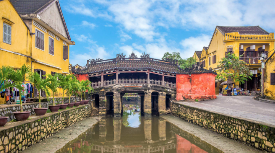 越南會安日本橋，歷史古橋橫跨水道，兩側黃色老房子映襯藍天