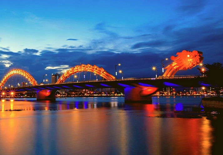 越南峴港龍橋夜景，橋身燈光璀璨映照於河面，展現獨特地標之美